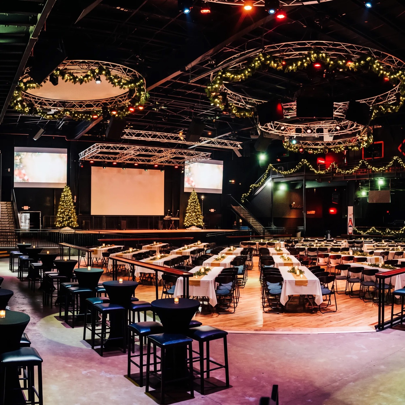 Escapade Event Center decorated for the holidays with garland-wrapped lighting rings, Christmas trees, and banquet tables